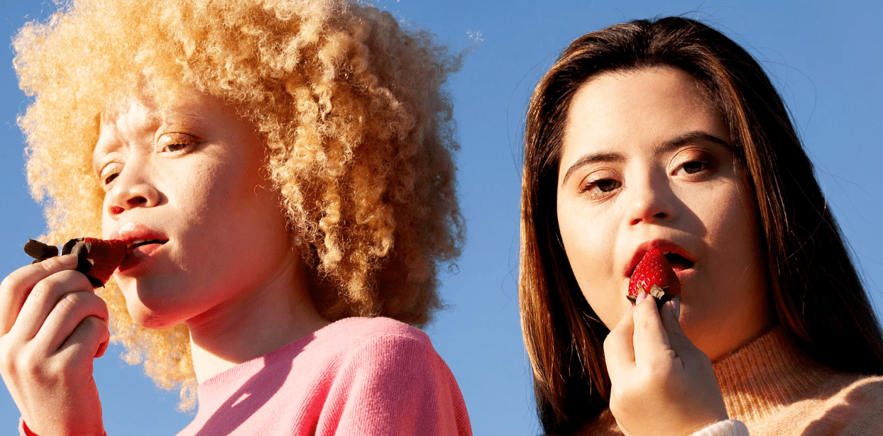 Two lesbians eating strawberries against a light blue background