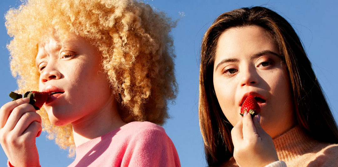 Two lesbians eating strawberries against a light blue background