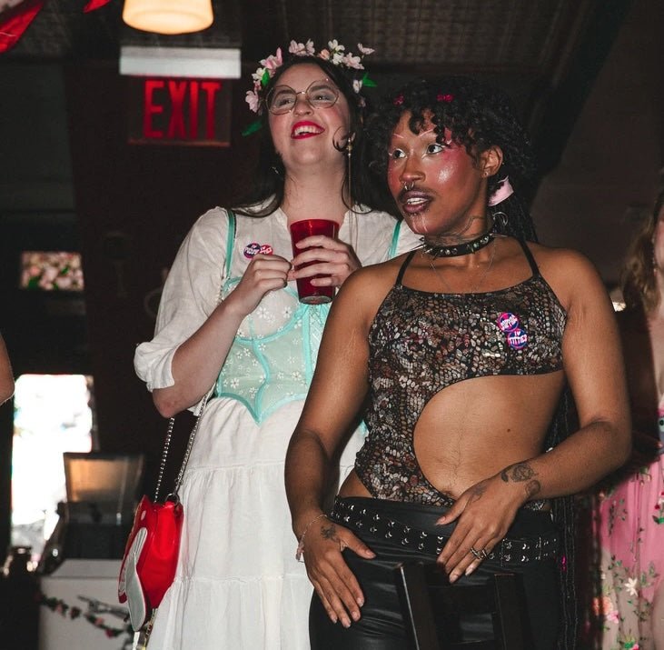 Person wearing a Pink and Blue Banana Split Pins that say "I  ❤ titties" and "sapphic."